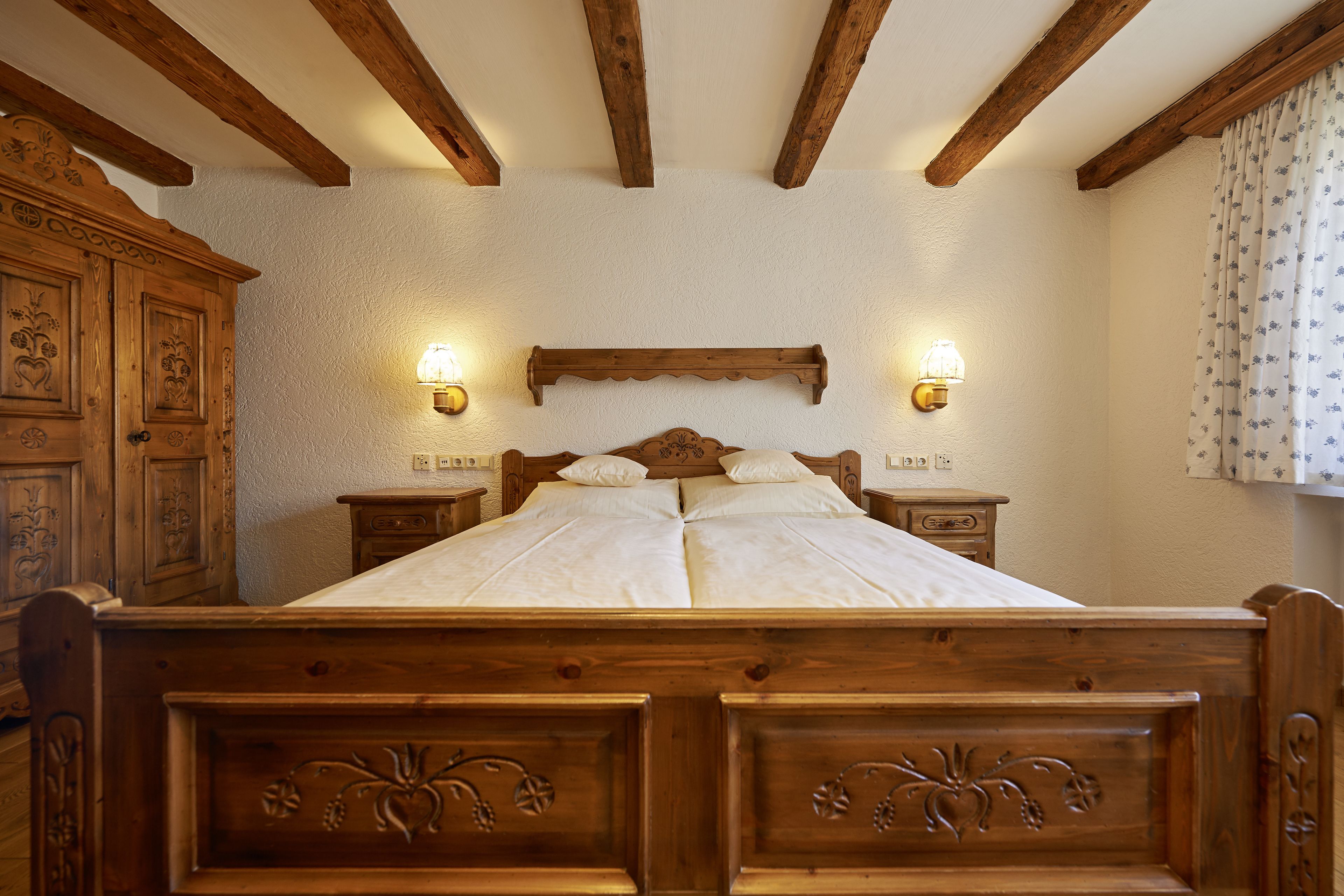 A wooden four-poster bed with a headboard, two bedside tables with lamps, and a wooden wardrobe.