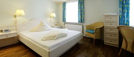 A hotel room with a bed, bedside lamps, a chair, a dresser, and a window with curtains.