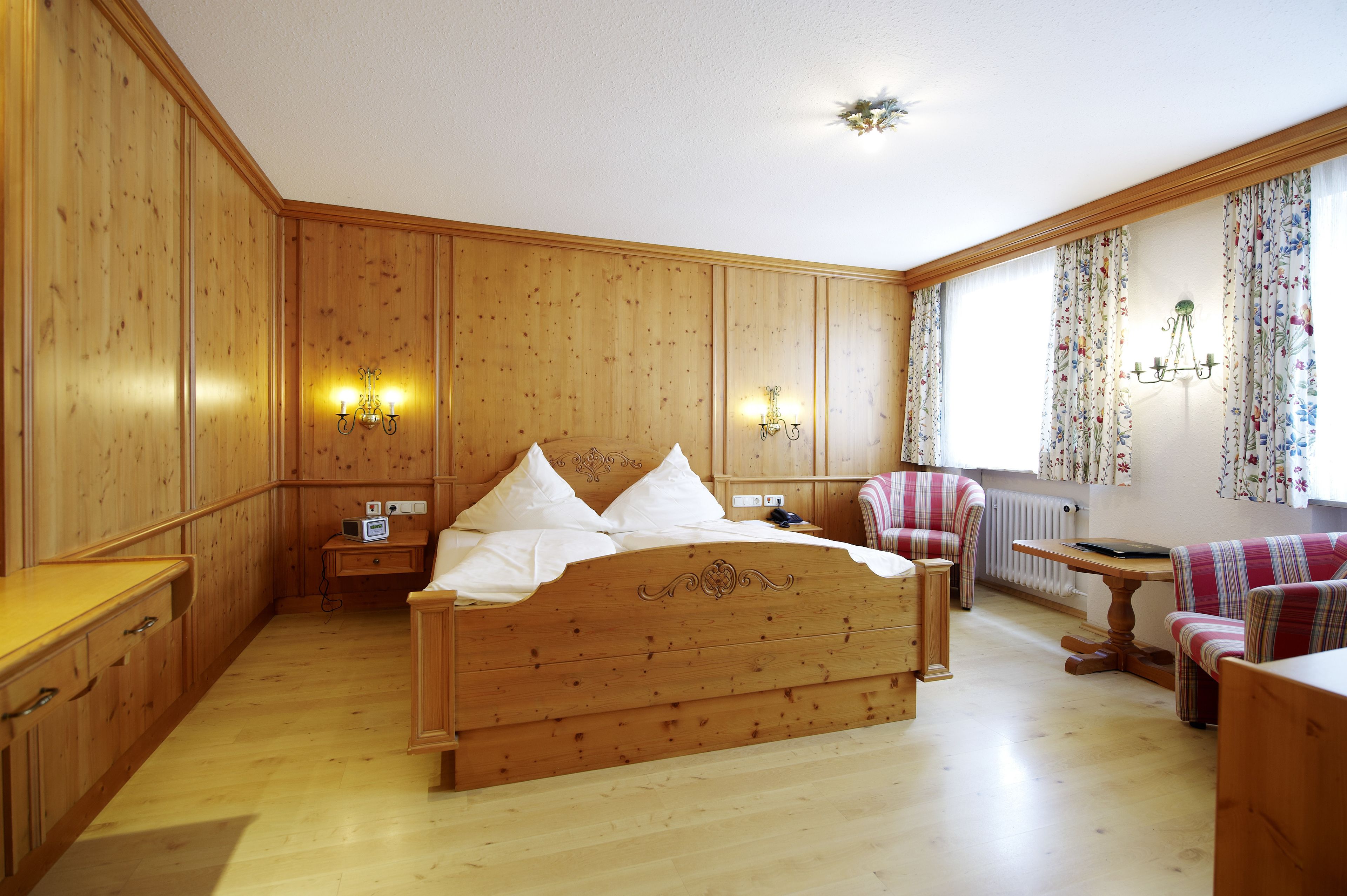 A wooden-paneled room with a bed, a chair, a table, and a radiator.