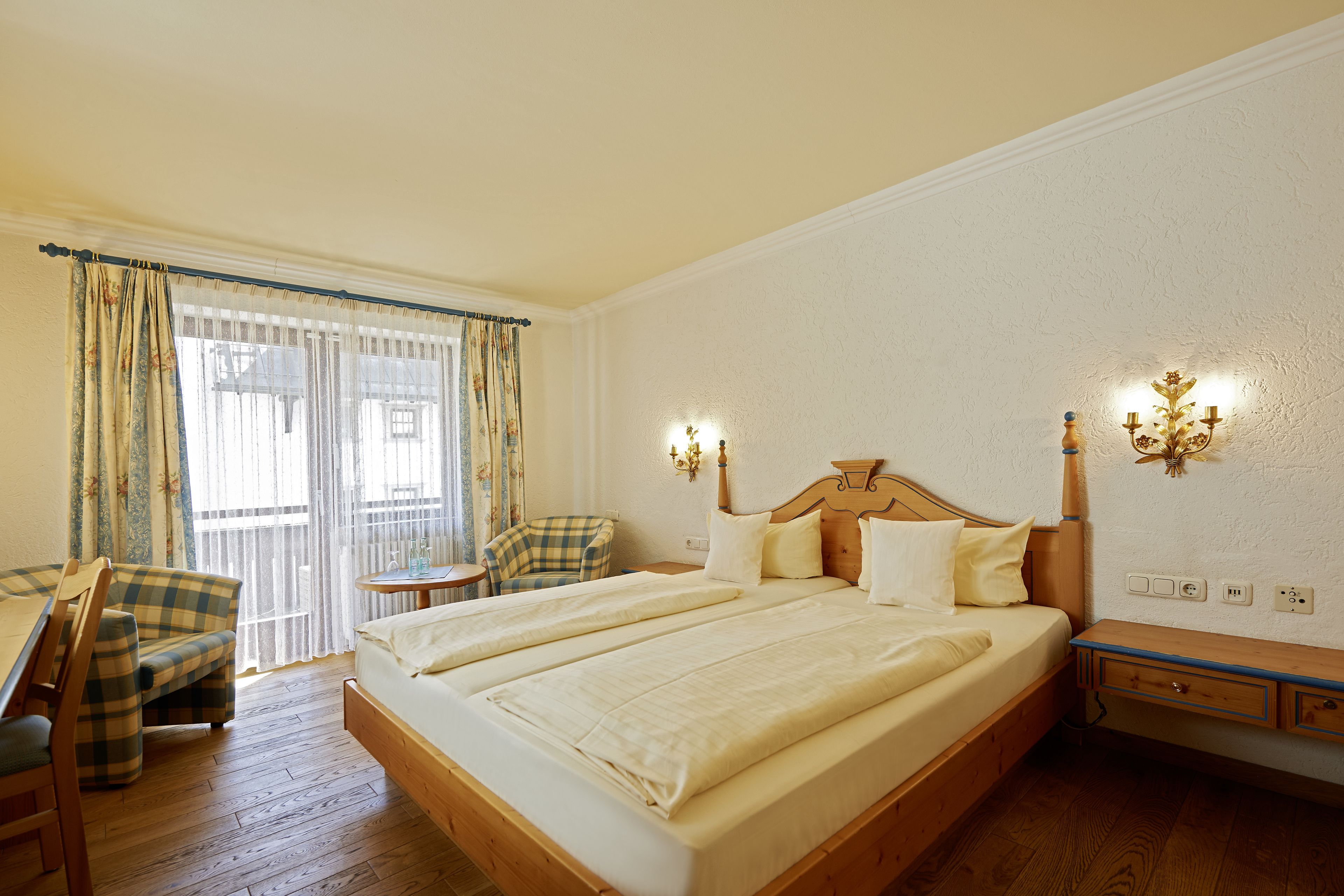 A double bed with a wooden headboard, a small bedside table, and a chair with a plaid cushion.