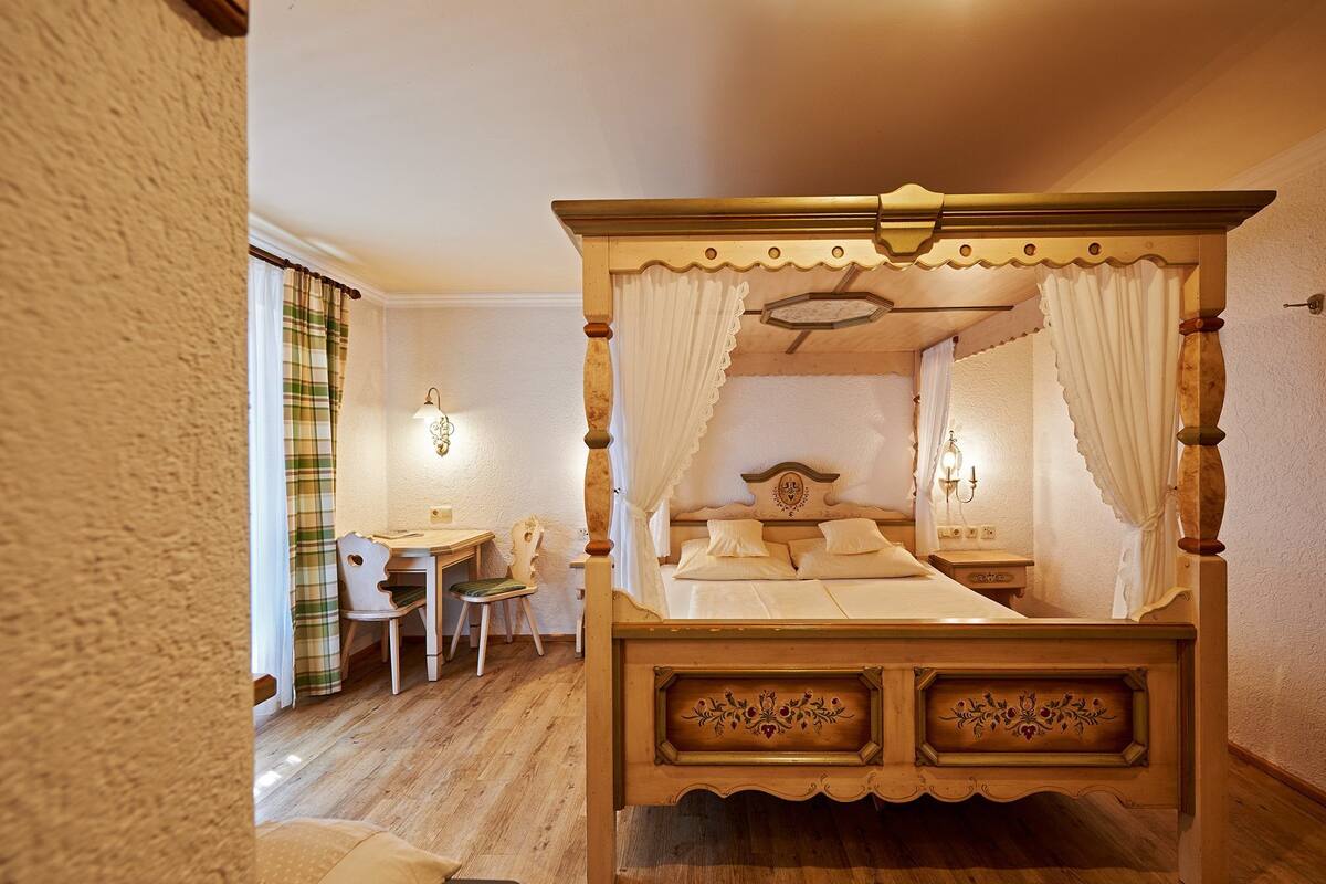 A four-poster bed with a canopy, a wooden desk, a chair, and a nightstand with a lamp.