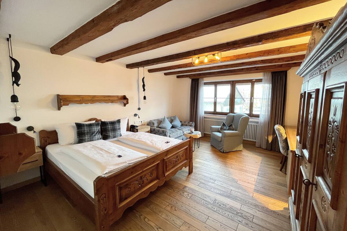 A traditional wooden bedroom with a large bed, a wooden dresser, and a window with curtains.