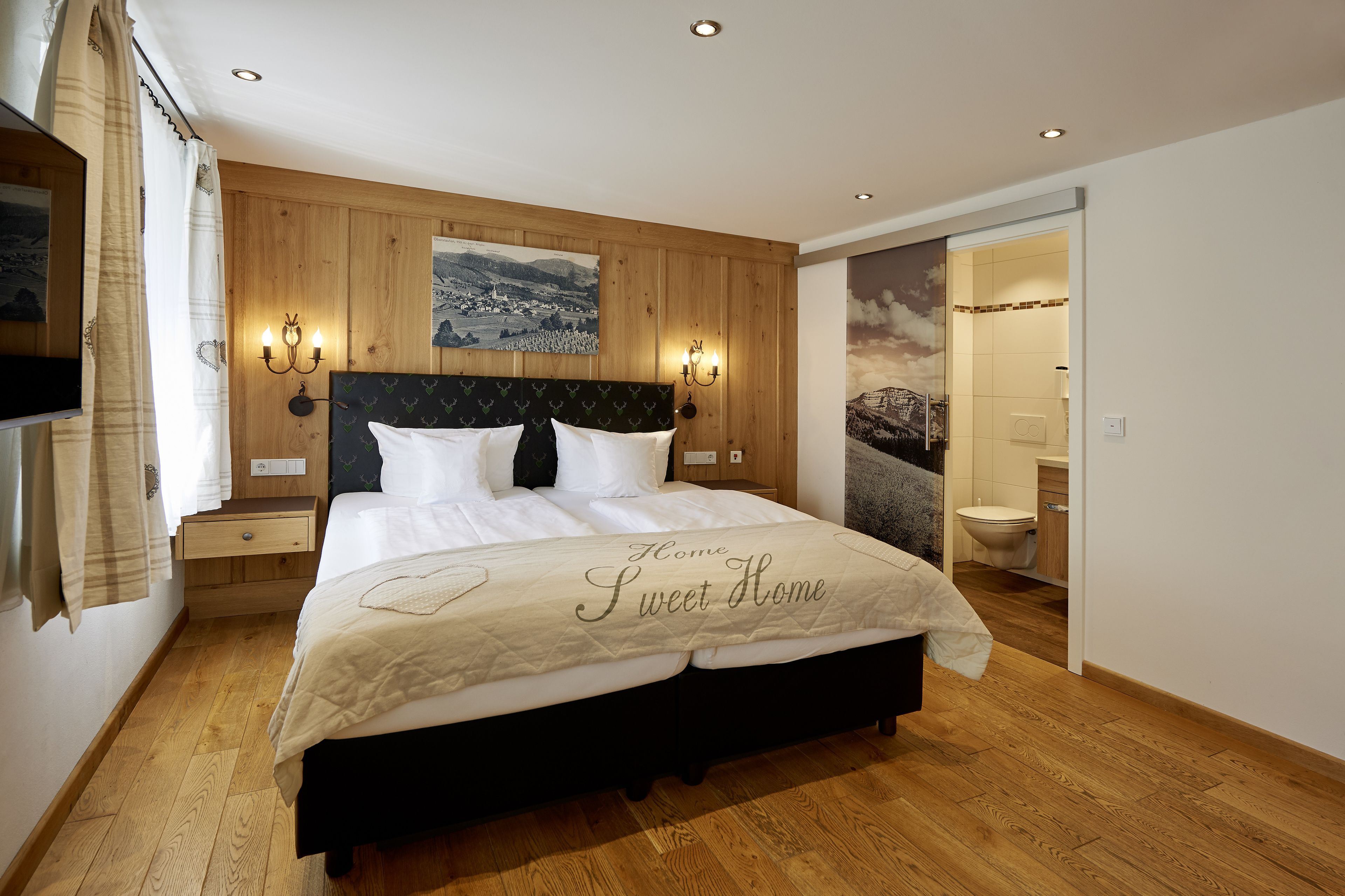 A bedroom with a wooden headboard, a bed with a white bedspread, a nightstand, a wall-mounted TV, and a painting above the bed.