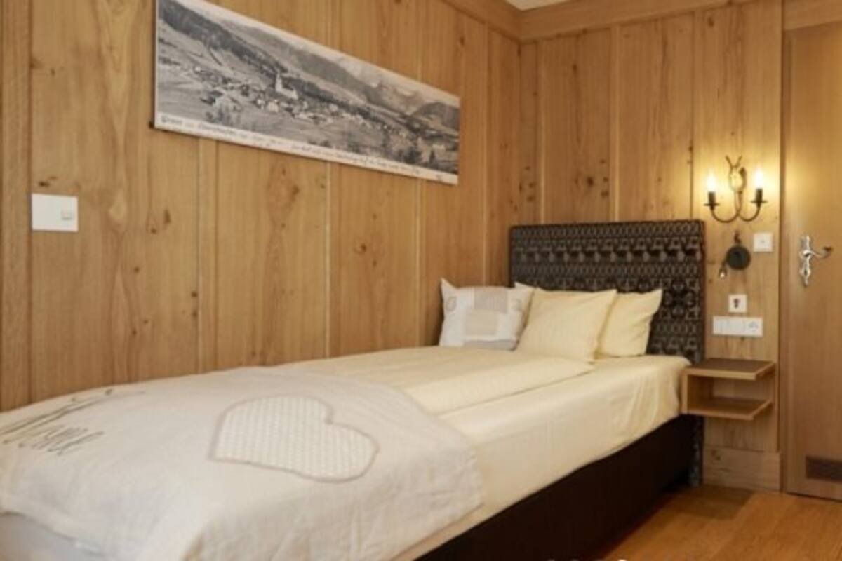A wooden-paneled room with a bed, a nightstand, a lamp, and a chair.