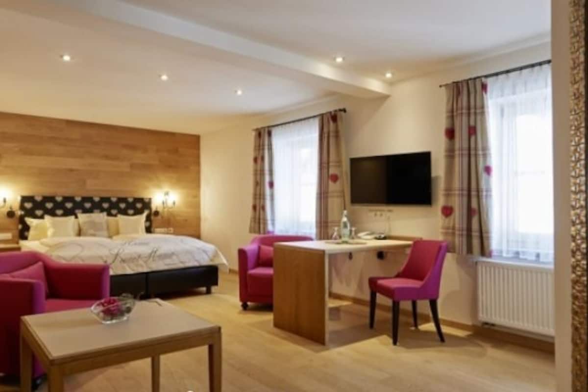A hotel room with two beds, a desk, a chair, a small table, and a TV.