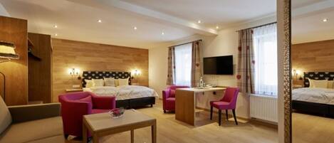 A hotel room with two beds, a desk, a chair, a small table, and a TV.