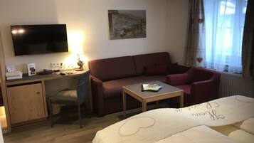 Ein Hotelzimmer mit Bett, Schreibtisch mit Computer, Sofa, Fernseher und Fenster mit Vorhängen.