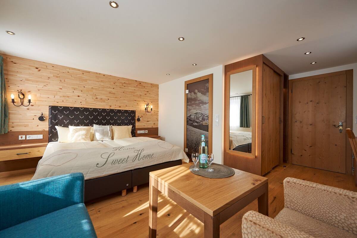 A bedroom with a bed, bedside tables, a mirror, a wooden floor, and a wooden wardrobe.