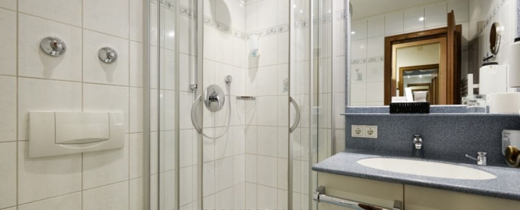 Un baño moderno con cabina de ducha de vidrio, un lavamanos blanco y un espejo grande.
