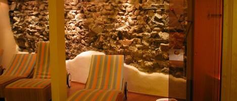 A room with two wicker lounge chairs, a stone wall, and a wooden door.