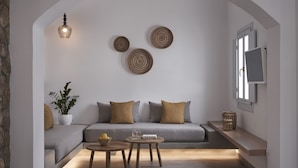 A modern living room with a grey sofa, two round wall decorations, a potted plant, and a small table with a bowl. - Makris Beach Hotel (Santorini)