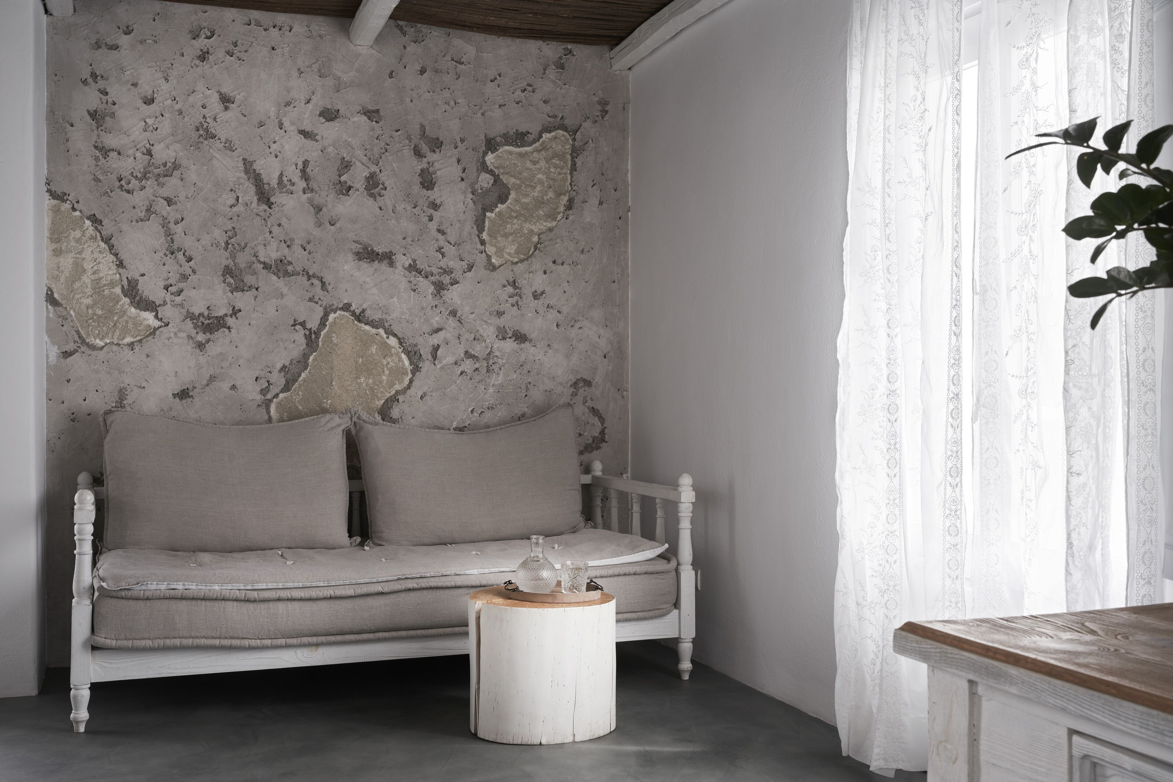 A room with a white sofa against a textured wall, a round wooden side table, and a white curtain with floral patterns.