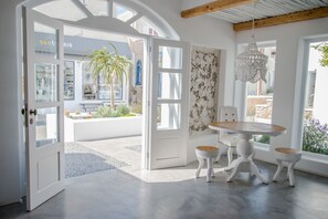 An open door leading to a patio with a table and chairs, a hanging light fixture, and a view of the outside. - Makris Beach Hotel (Santorini)