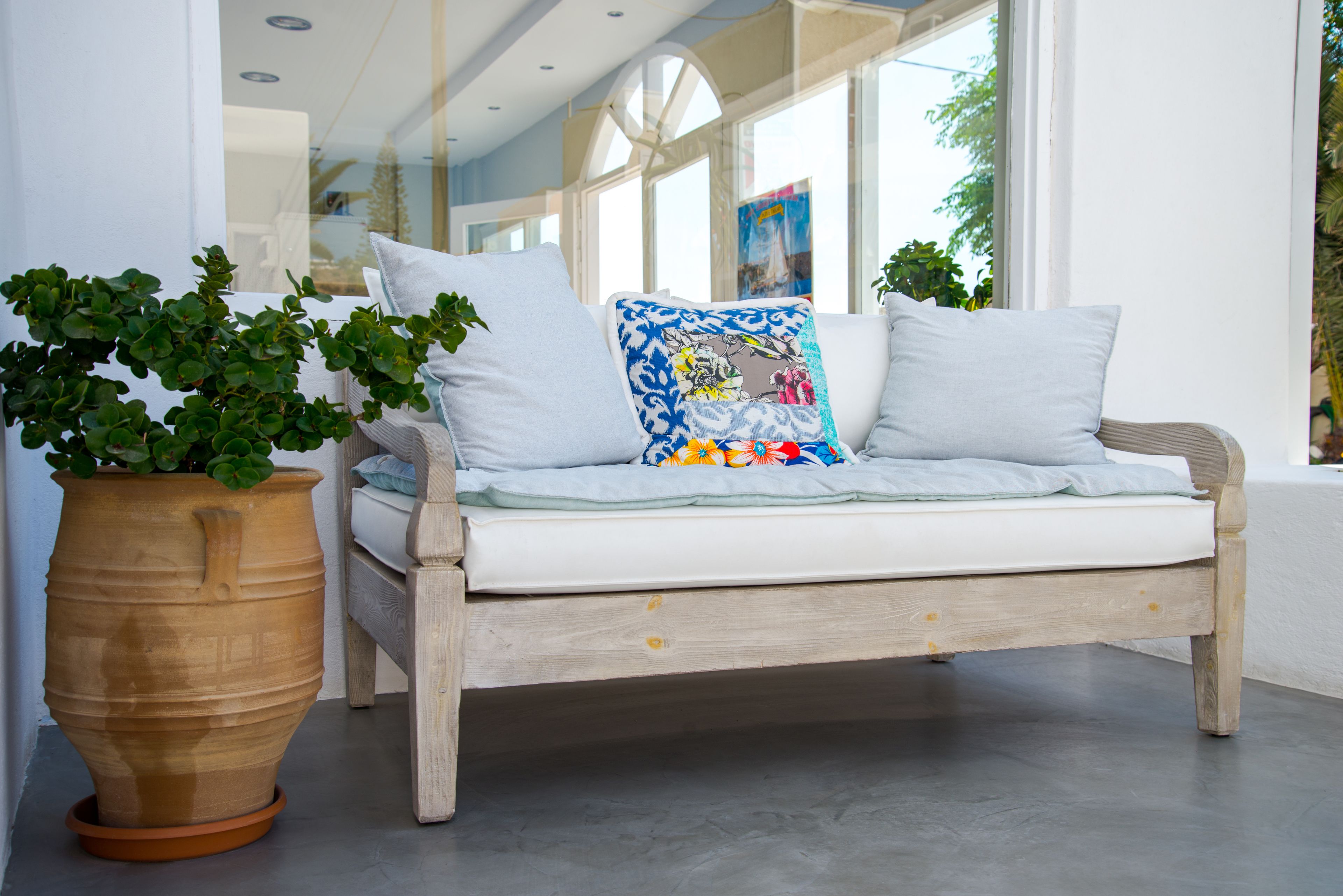 A wooden bench with cushions and a potted plant beside it.