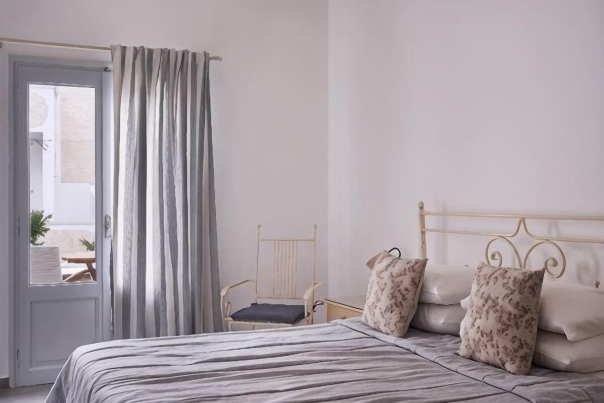 A bedroom with a bed, curtains, a chair, and a view of the outside.