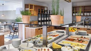 Een buffet met diverse gerechten, waaronder fruit, kazen en vlees, in een moderne keuken met houten kasten en plantenbakken.