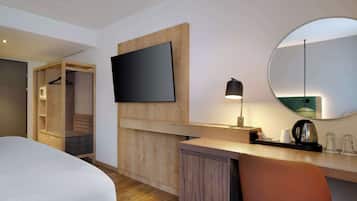 A hotel room with a bed, a desk with a lamp, a flat-screen TV, a mirror, and a walk-in closet.