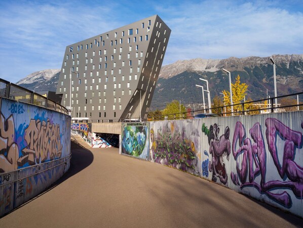 Un edificio moderno con un diseño angular distintivo, rodeado de paredes cubiertas de grafitis y un paisaje montañoso.