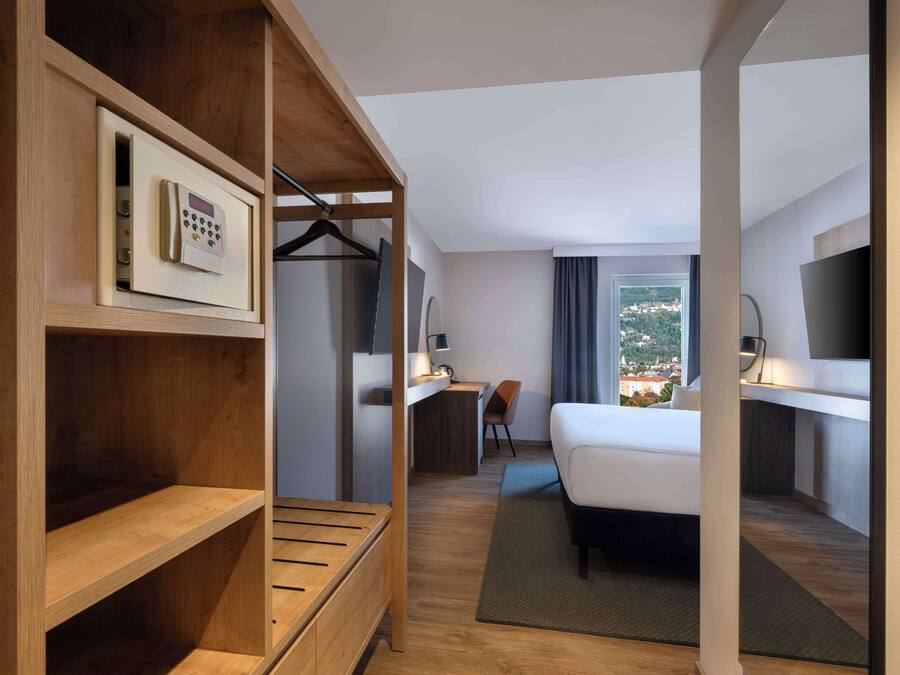 A hotel room with a bed, desk, chair, and a view of the city.