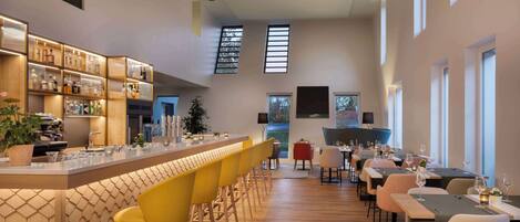 A modern bar area with a long counter, yellow bar stools, and a variety of bottles and glasses.