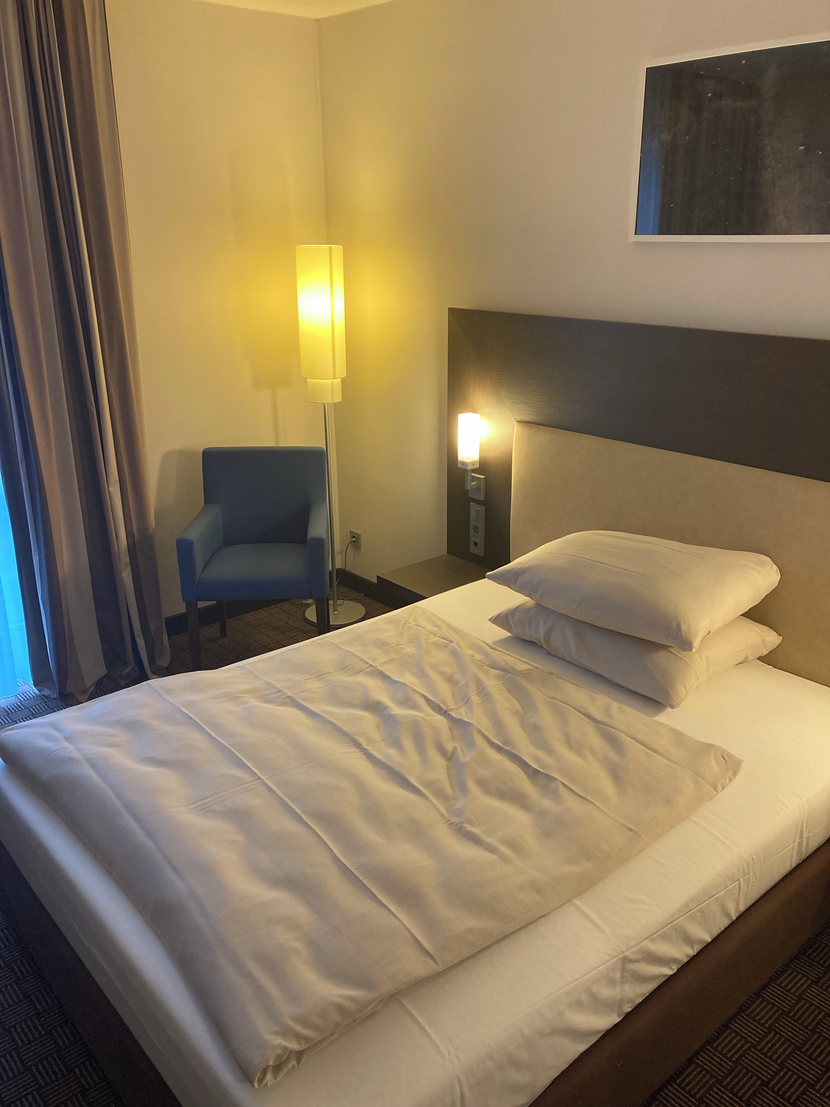 Una habitación de hotel con una cama, una silla, una lámpara y una lámpara de pared.