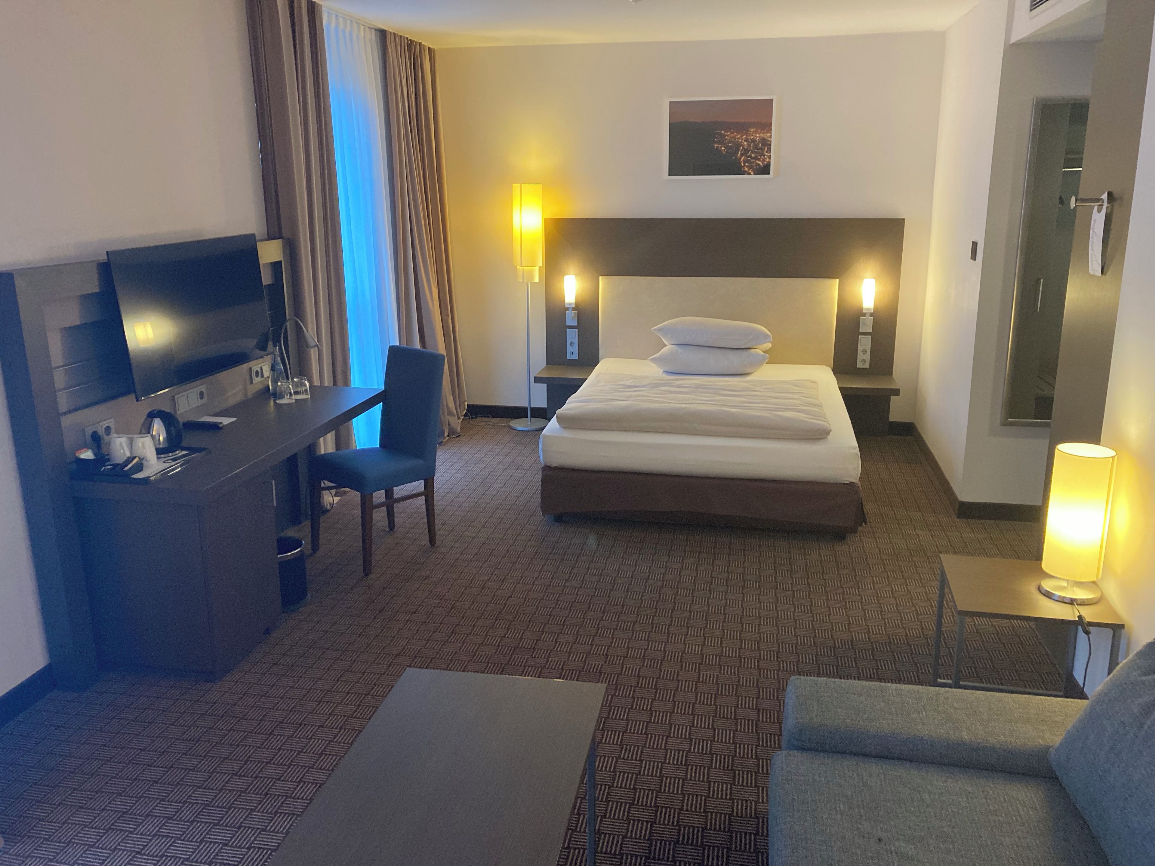 Habitación de hotel con una cama, un escritorio, una silla, un televisor y una lámpara.