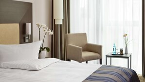 A hotel room with a bed, a chair, a small table with a vase and a bottle, and a large window with curtains. - IntercityHotel Bonn (Bonn)