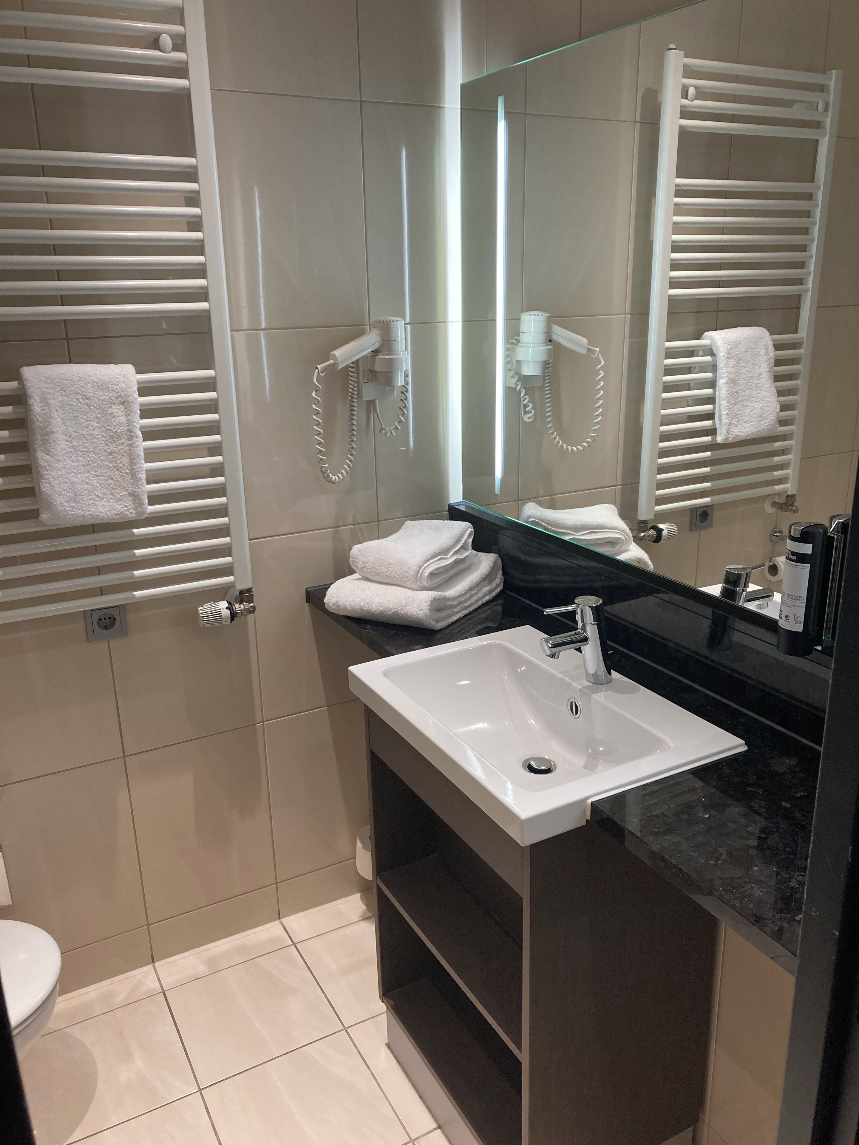A modern bathroom with a white sink, a mirror, and towel racks.