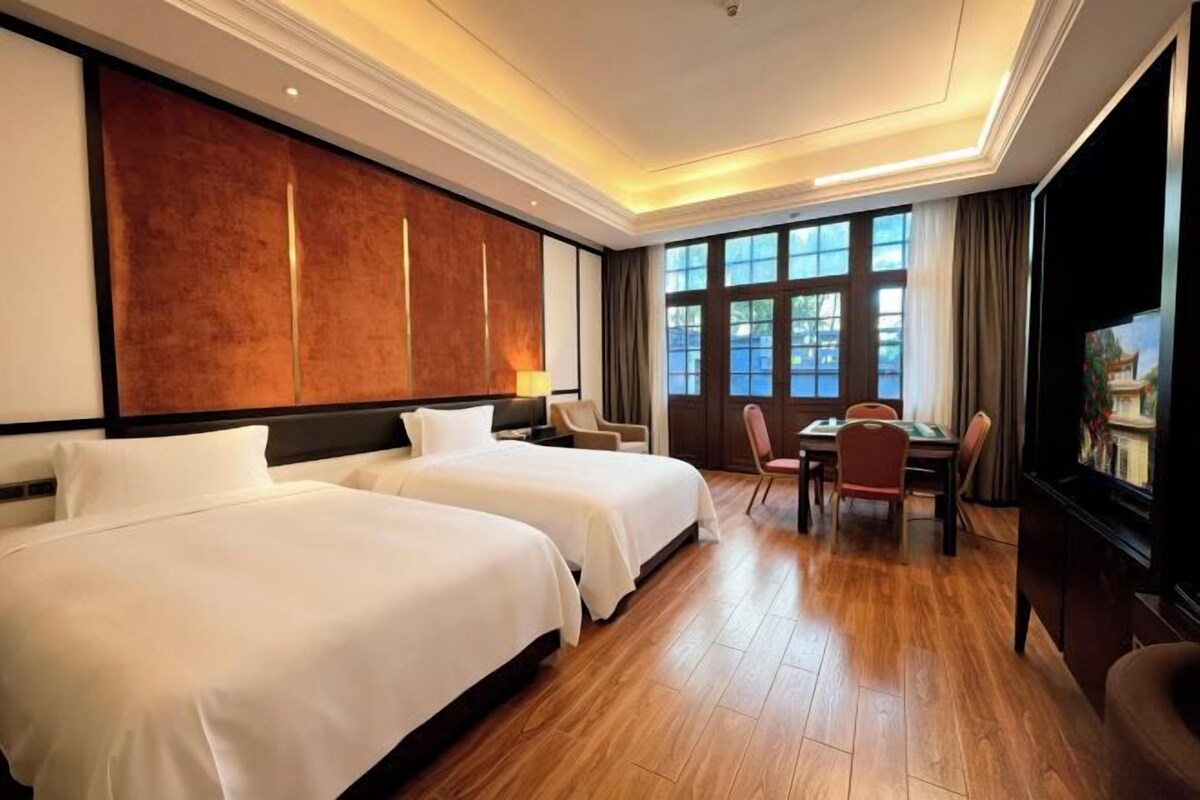 Ein Hotelzimmer mit zwei Betten, einem Esstisch, Stühlen, einem Fernseher und großen Fenstern.