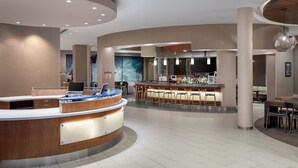 Un moderno vestíbulo de hotel con una recepción, una zona de bar y un espacio de descanso.