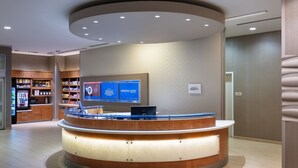 Zona de recepción de un hotel con un mostrador curvo, una pantalla digital que muestra opciones de habitaciones y un interior bien iluminado.