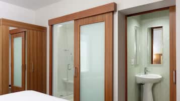 Un baño moderno con cabina de ducha de vidrio, un lavabo blanco y puertas de madera.