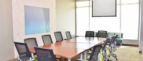 Un salón de conferencias con una gran mesa, sillas, una pantalla de proyector y un amplio ventanal.