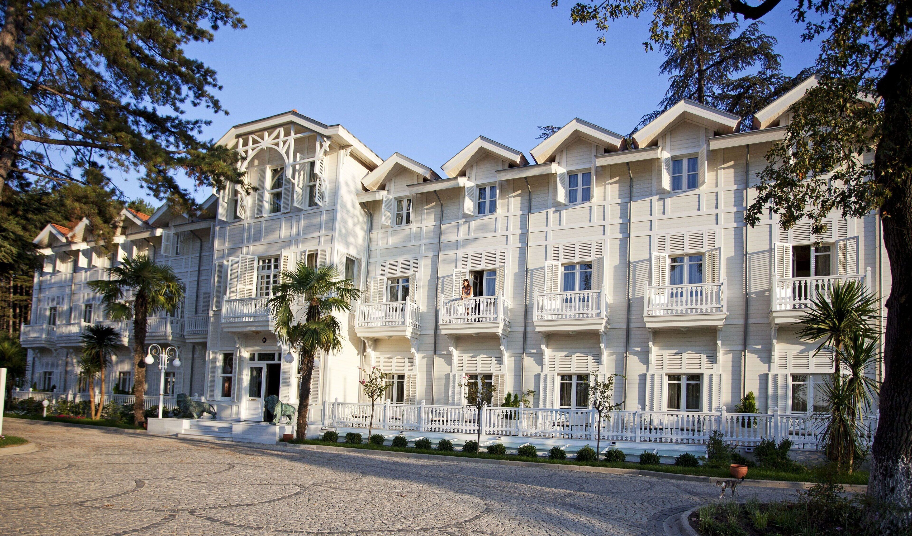 Un hotel de varios pisos con balcones, un camino de adoquinado y palmeras.