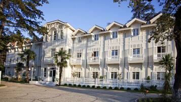 Un hotel de varios pisos con balcones, un camino de adoquinado y palmeras.