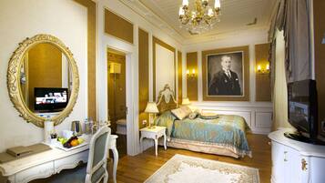 A luxurious bedroom with a large bed, a desk, a television, and a portrait on the wall.