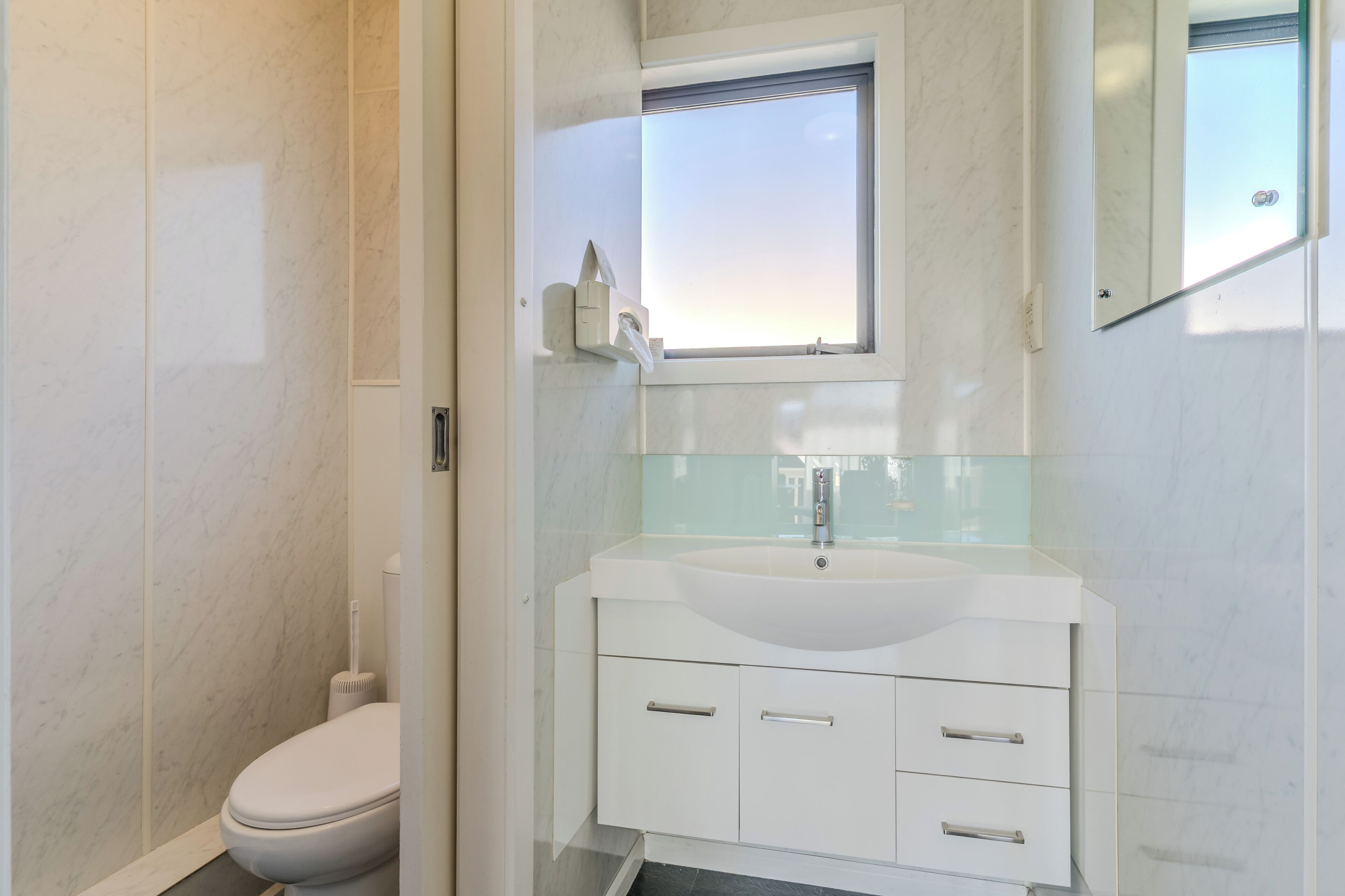 A modern bathroom with a white sink, mirror, and toilet.