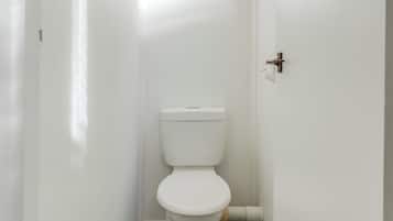 A small, white bathroom with a toilet, a white door, and a light switch on the wall.