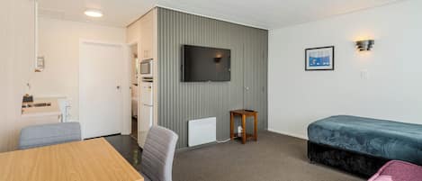 Een knus kamer met een bed, een aan de muur bevestigde televisie, een klein tafeltje en een kitchenette.