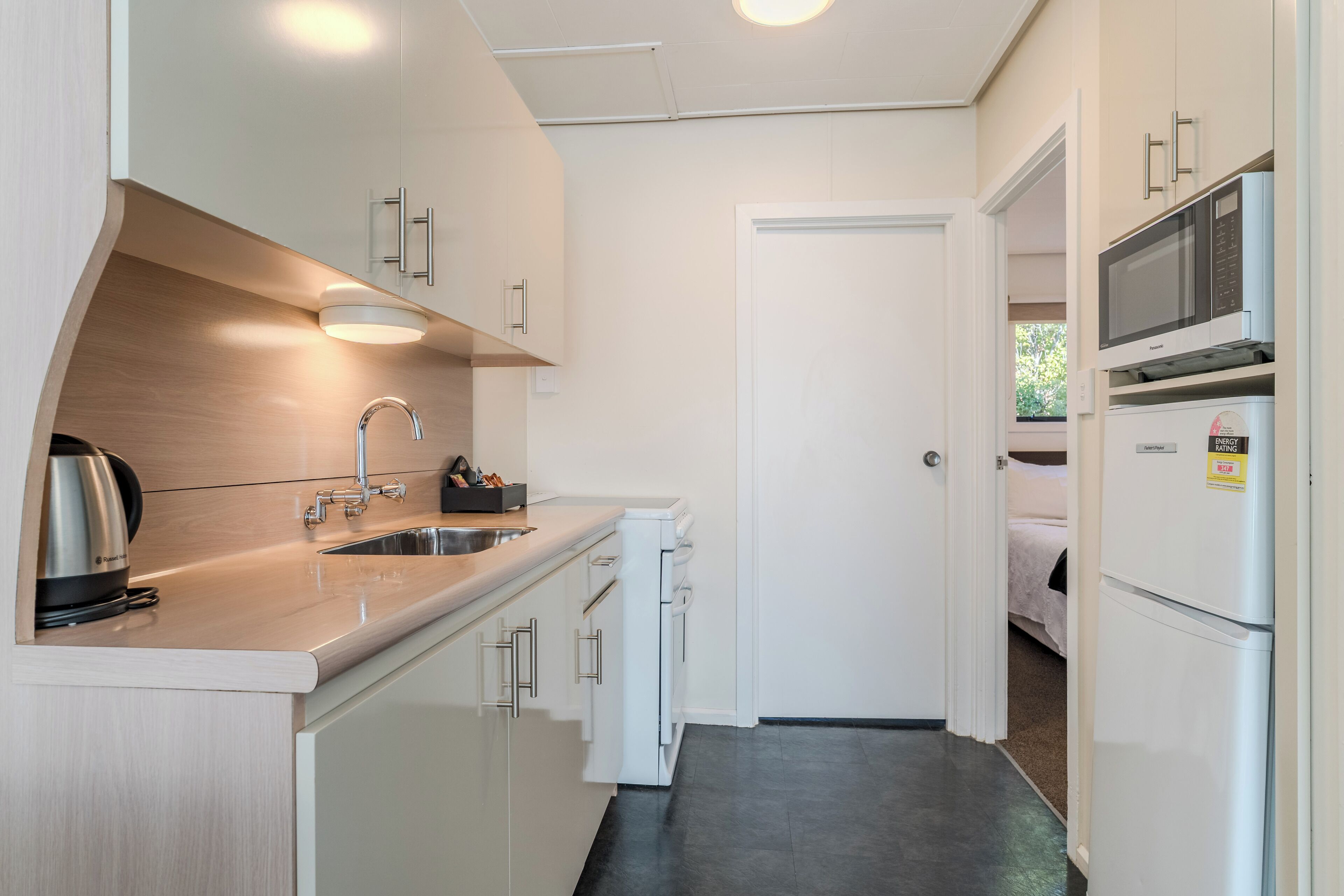 A compact kitchen with white cabinetry, a stainless steel sink, a microwave, and a refrigerator.