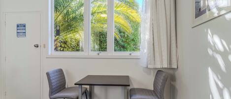 A room with a window, two chairs, a table, a door with a fire action notice, and a framed picture on the wall.