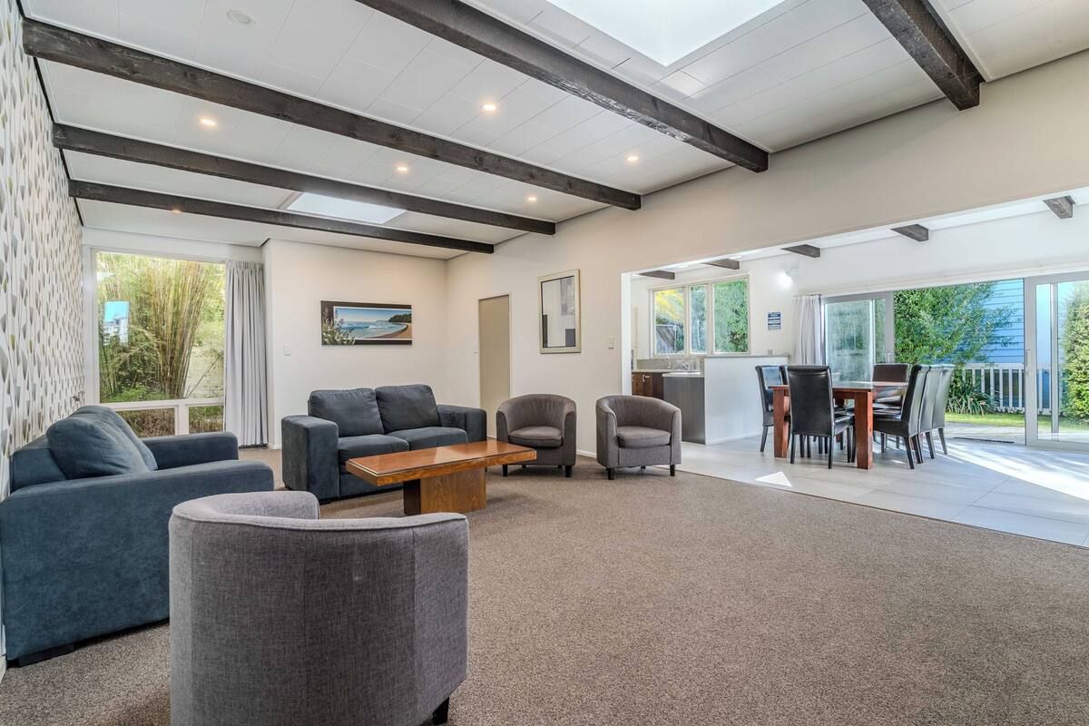 A spacious living area with a high ceiling, built-in wooden beams, and a large sliding glass door leading to an outdoor patio.