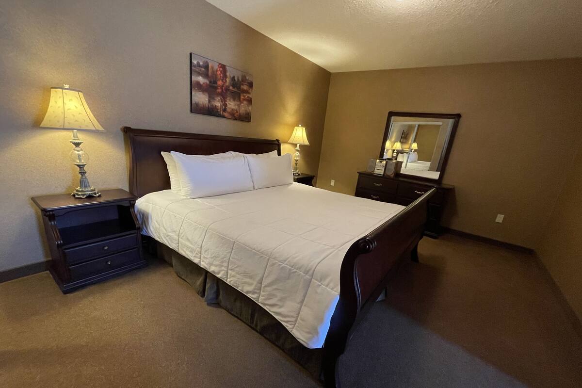 Habitación de hotel con una cama grande, dos mesitas de noche, una lámpara, un espejo y un cuadro en la pared.