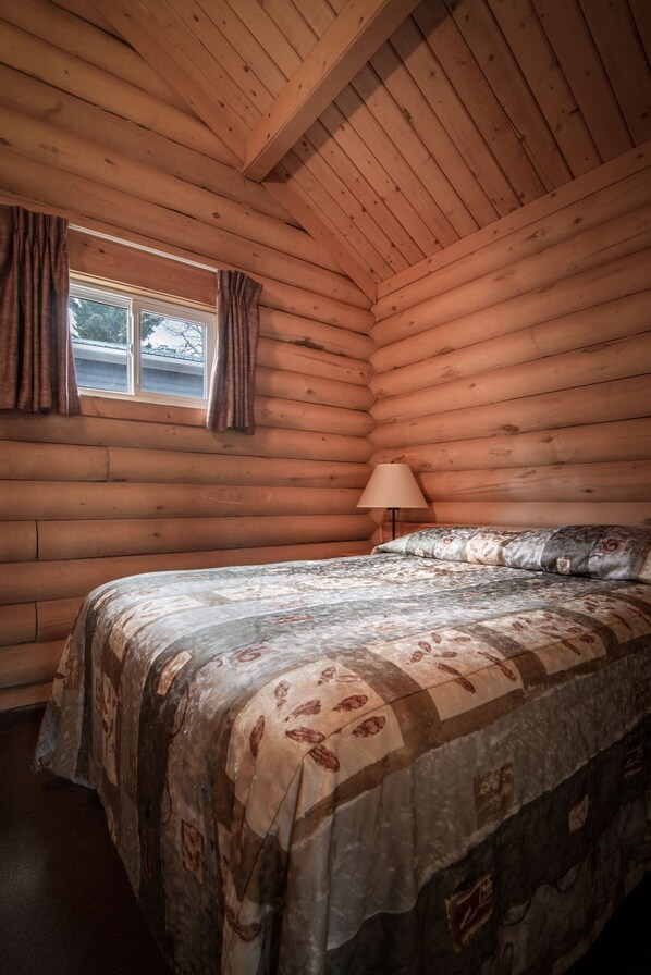 A log cabin bedroom with a bed, a lamp, and a window with curtains.