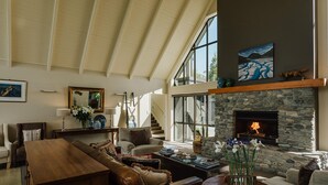 A spacious living room with a stone fireplace, large windows, and a high ceiling.