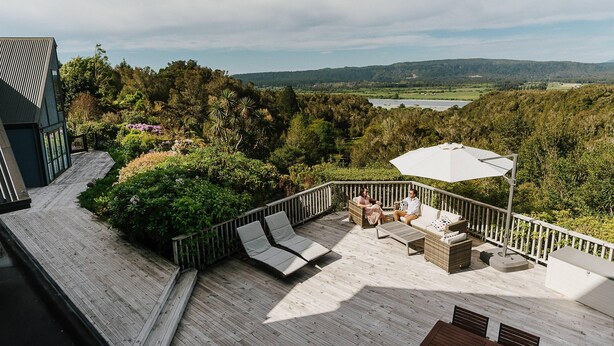 A deck with outdoor seating, a view of a lake, and surrounding greenery.