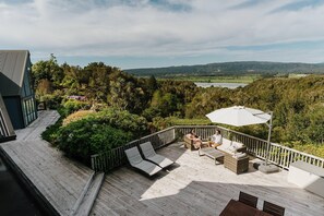 A deck with outdoor seating, a view of a lake, and surrounding greenery.