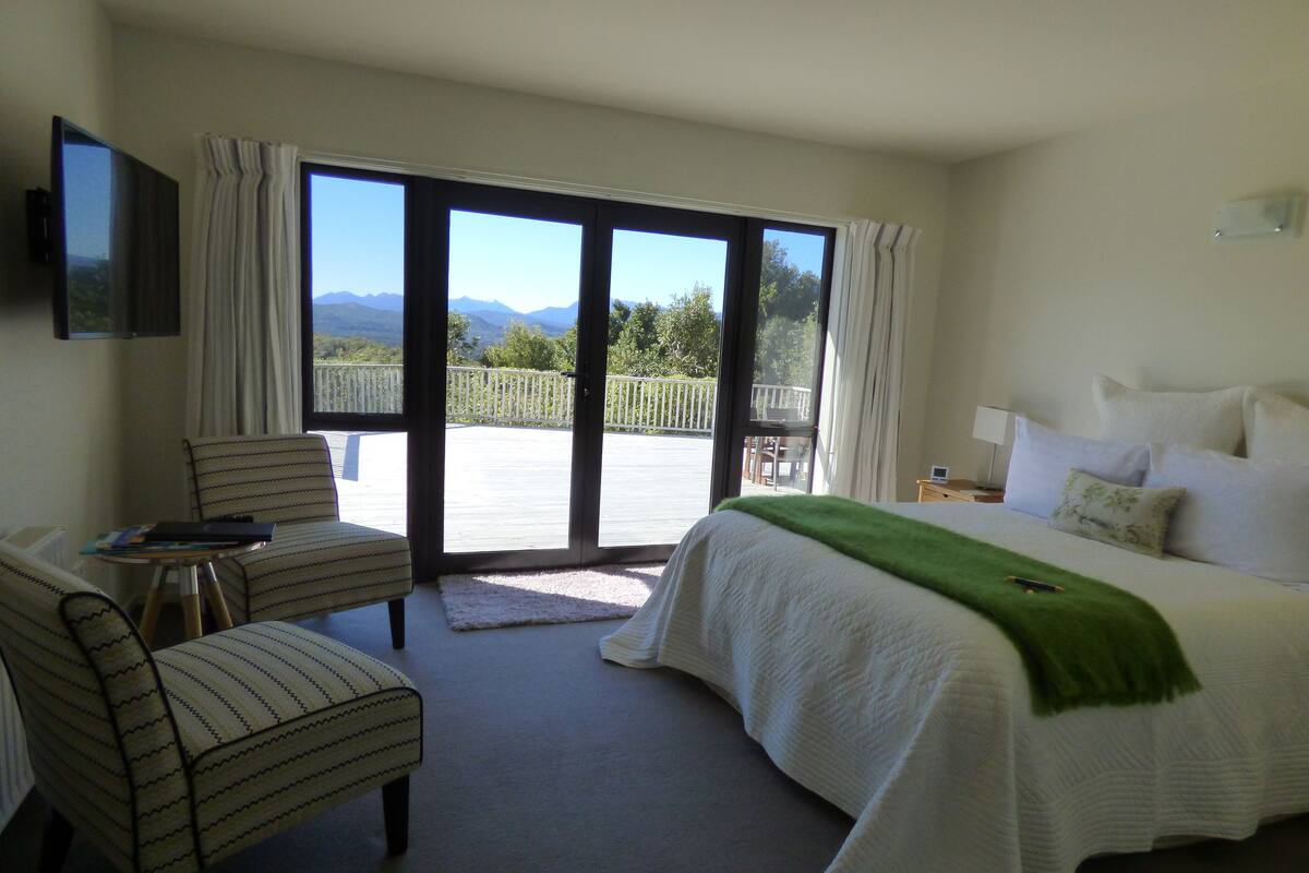 Et hotelværelse med en seng, en stol, et lille bord og en balkon med udsigt til bjerge.