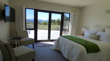 A hotel room with a bed, a chair, a small table, and a balcony with a view of mountains.