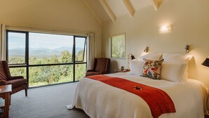 A bedroom with a large window, a bed with white bedding, a red throw blanket, and a chair.